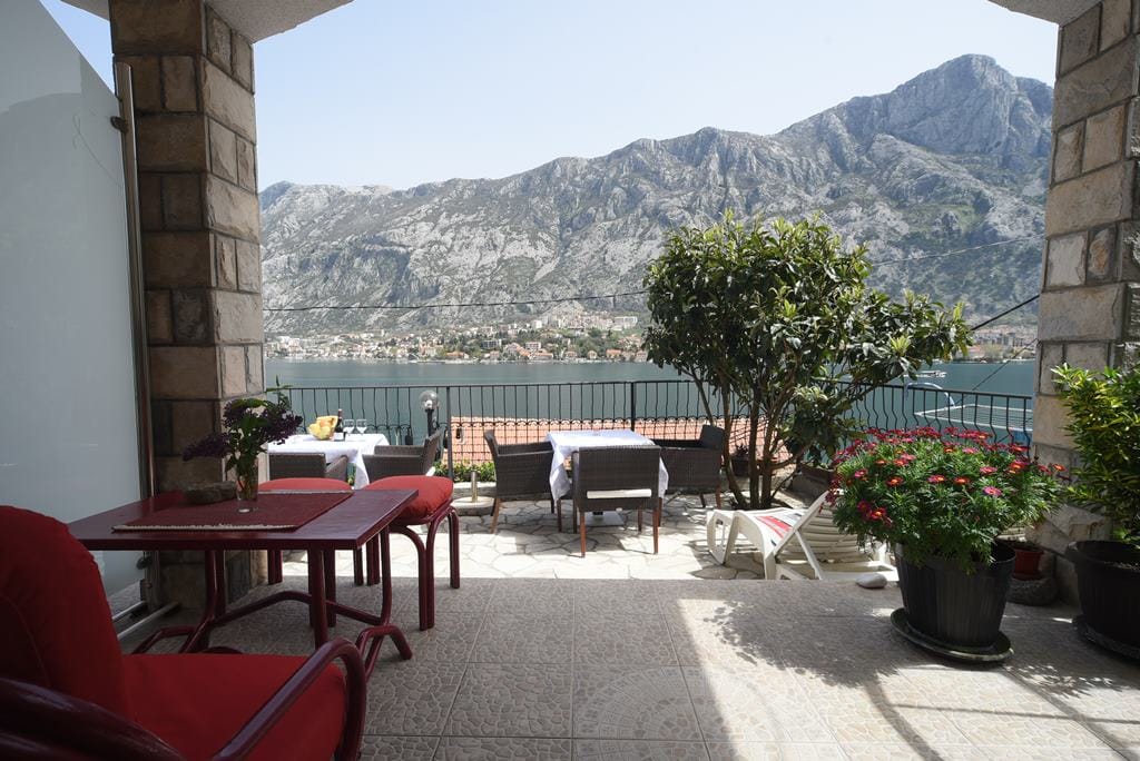 Terrace with a view of the Bay of Kotor and the mountains in a house, Muo, Montenegro: wicker furniture, stone finishes, and flowers.