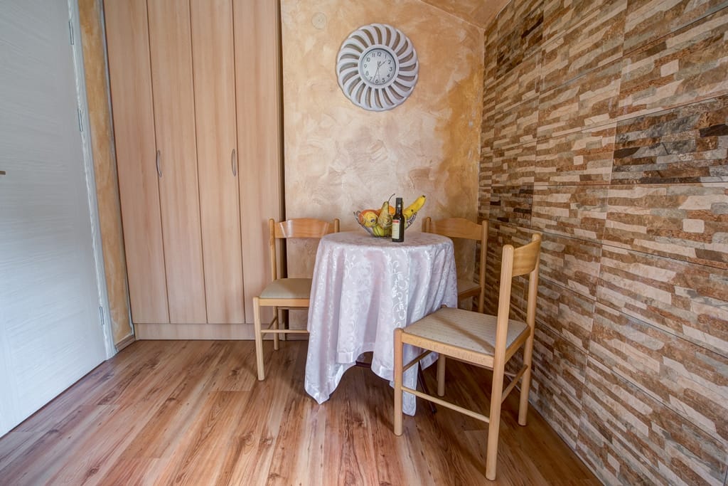 Dining area in the living room of a house in Muo, Montenegro: wooden chairs, a table with a cover, and decorative stone wall finish.