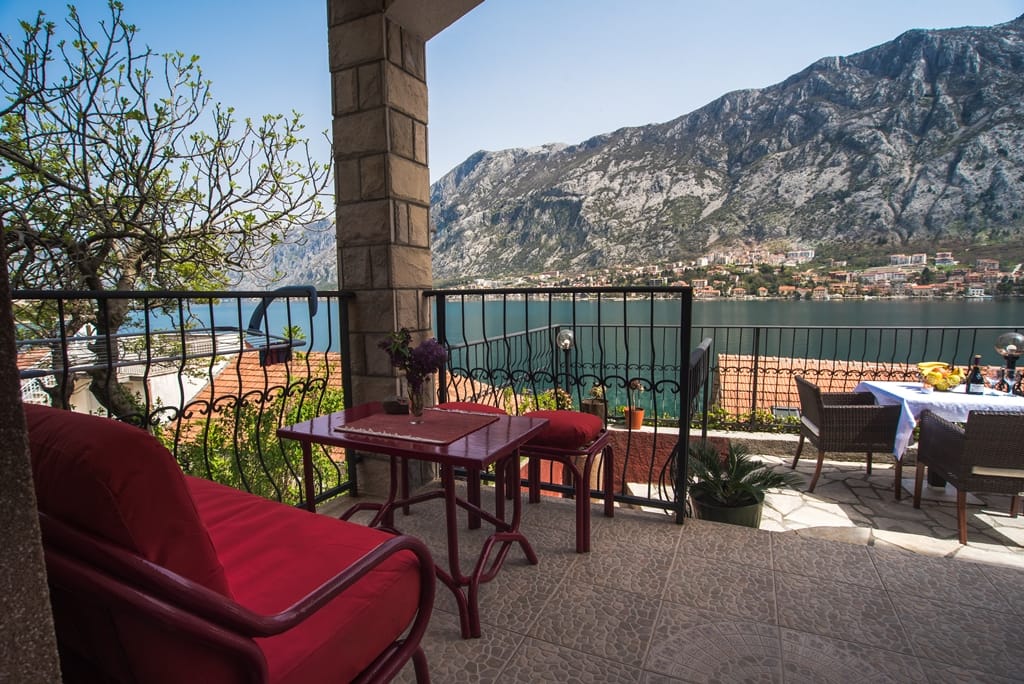 Terrace with furniture and a view of the Bay of Kotor, house in Muo, Montenegro: stone finish, table and chairs on the balcony.