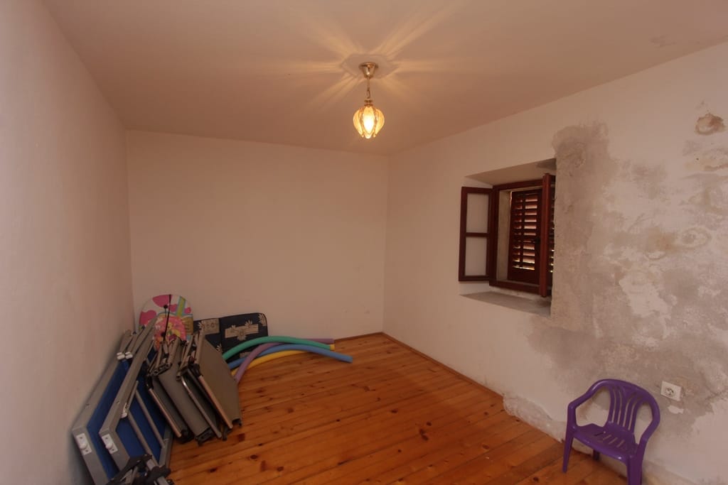 Room with a wooden floor and a window with shutters in a house for sale, Prčanj, Montenegro. Needs cosmetic renovation.