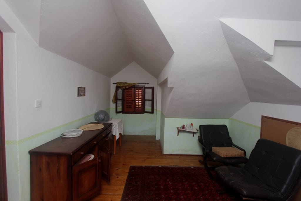 Living room in the attic of a house in Prčanj, Montenegro: wooden floor, vintage furniture, shuttered window, and sloped ceiling.