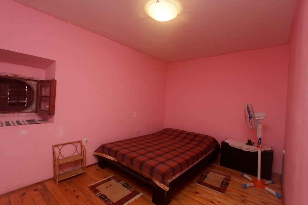 Bedroom in a house in Prčanj, Montenegro: double bed, wooden floor, pink walls, and a small window.