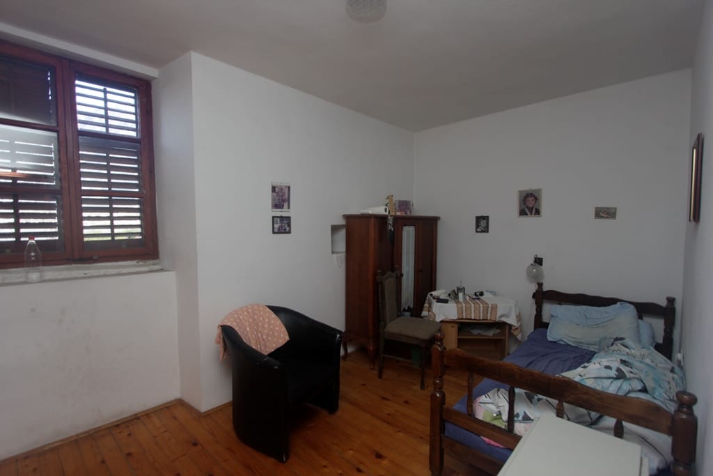 Bedroom in a house in Prčanj, Montenegro: wooden floor, bed, vintage wardrobe, armchair, and window with wooden shutters.