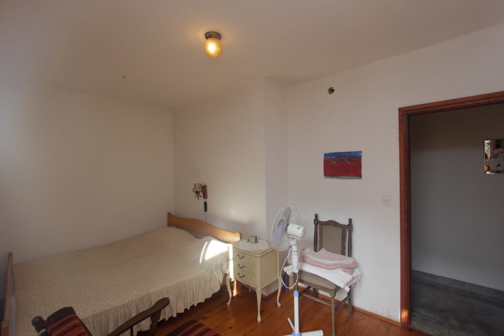 Bedroom in a house in Prčanj, Montenegro: wooden bed, vintage nightstand, floor fan, and parquet flooring.