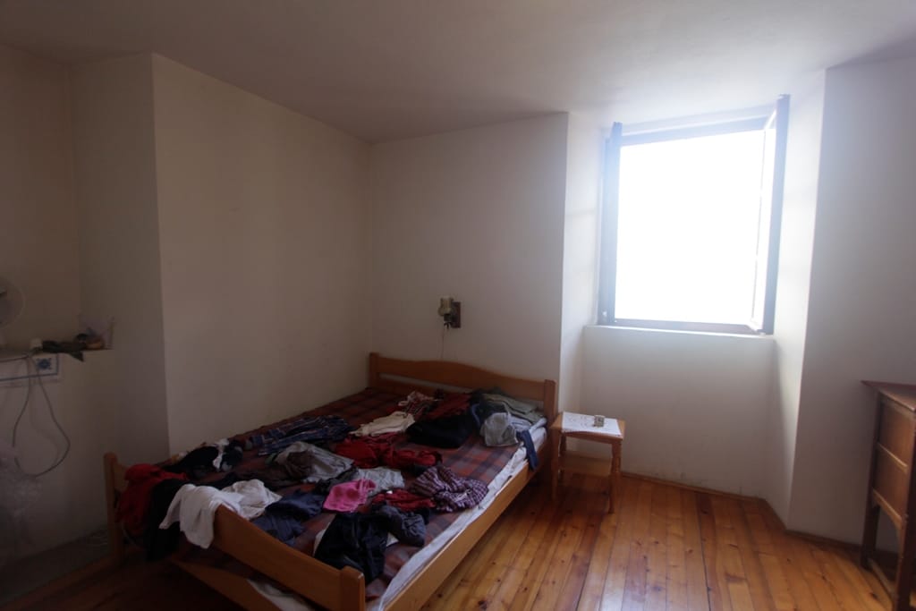 Bedroom with a wooden bed and floor in a house for sale in Prčanj, Montenegro, a bright room with a window.