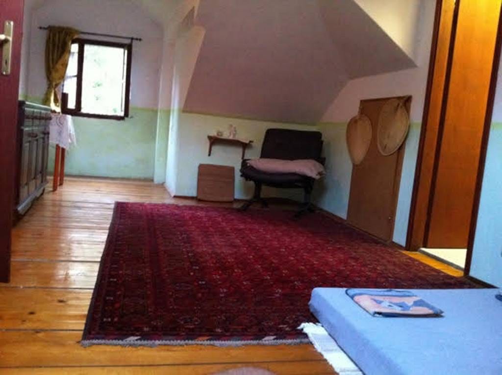 Living room in the attic of a house in Prčanj, Montenegro: wooden floor, red rug, armchair, and a window with a view.