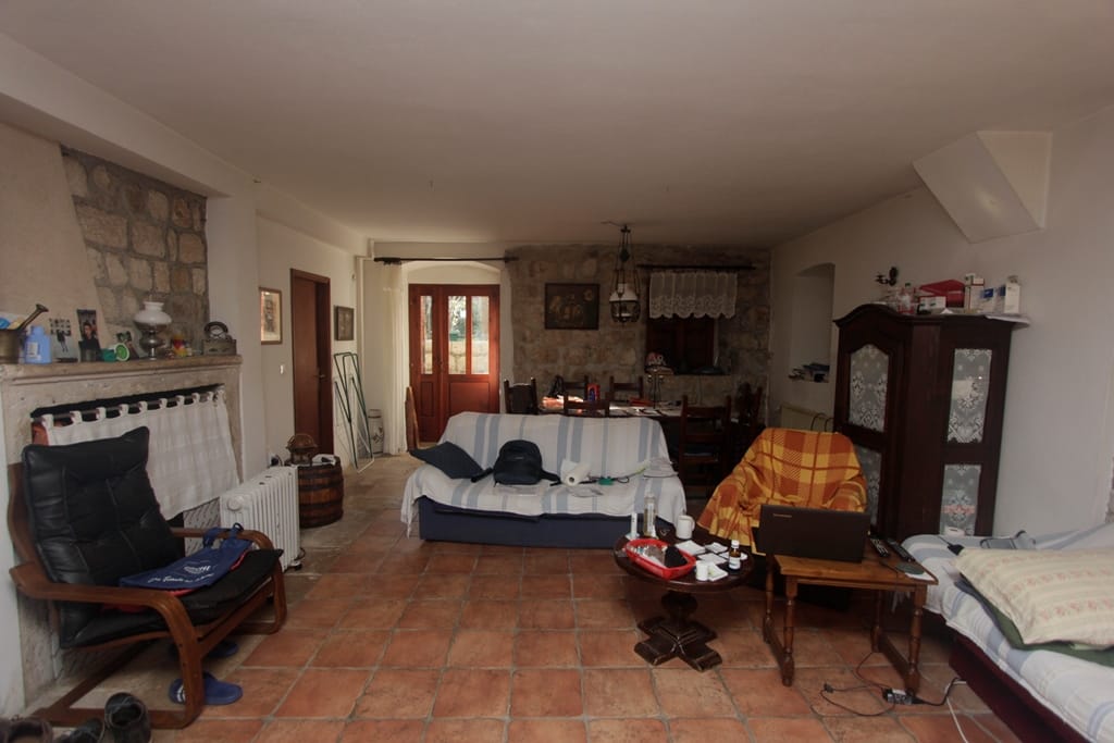 Living room in a house in Prčanj, Montenegro: stone walls, terracotta floor, fireplace, wooden furniture, and dining area.