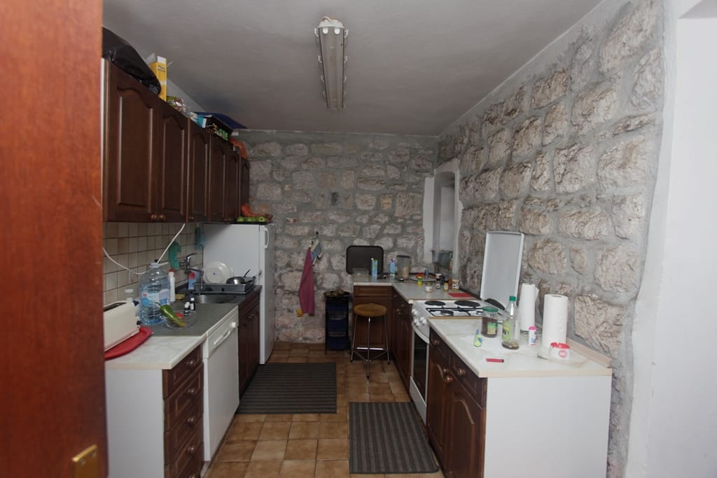 Kitchen in a house in Prčanj, Montenegro: brown cabinets, stove, and authentic stone wall finish in the interior.