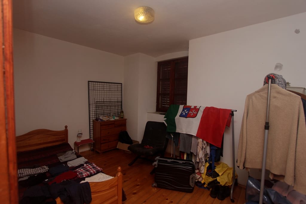Bedroom with a wooden bed and floor in a house for sale in Prčanj, Montenegro: interior view with furniture and a window.