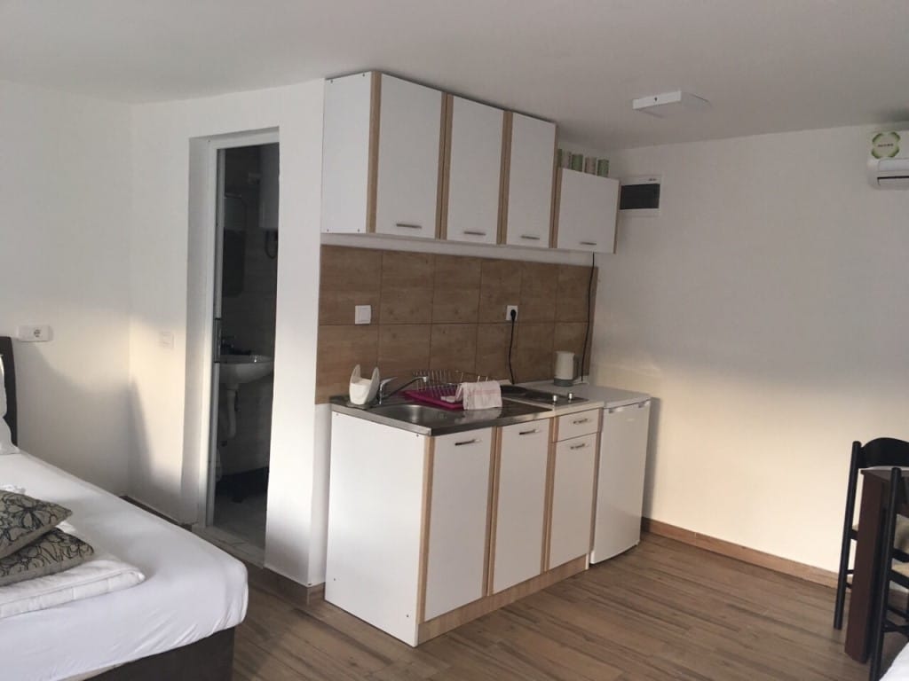 Kitchen in a mini-hotel room in Rafailovici, Montenegro: white furniture, wood-look backsplash, and a separate bathroom.