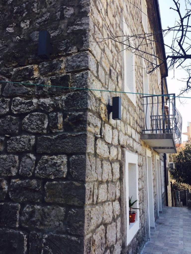 Facade of a mini-hotel made of natural stone with a balcony in Rafailovici, Montenegro: exterior view of a historic building.