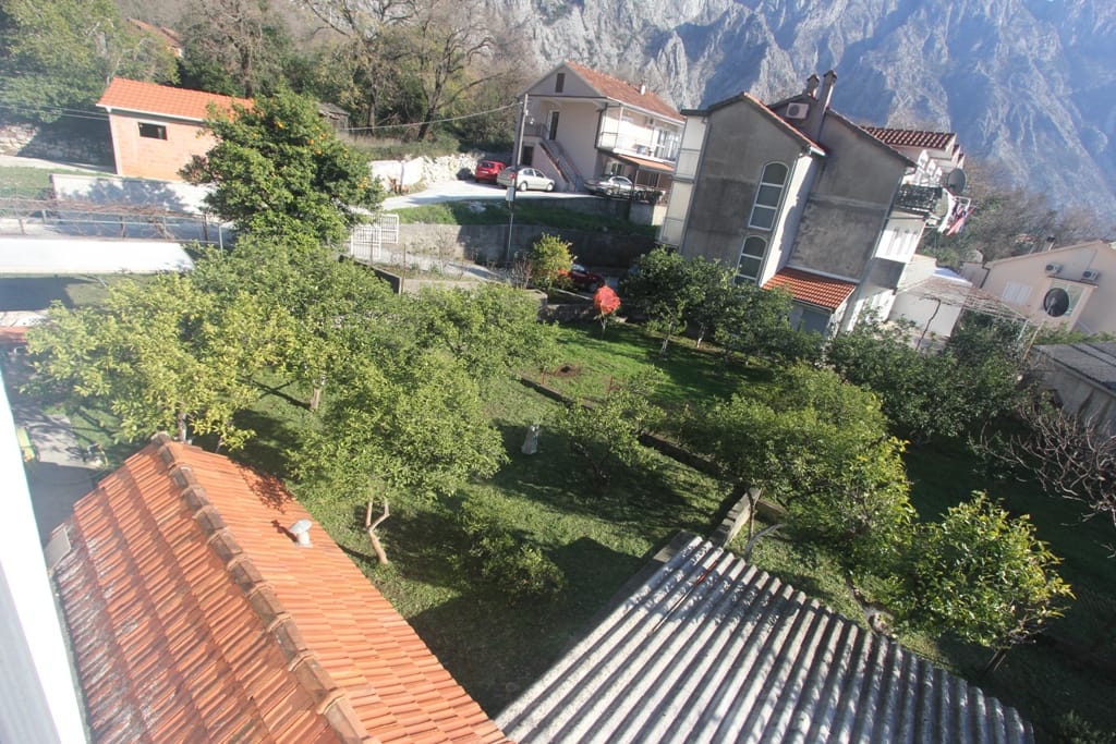 View of a green garden and mountains from the terrace of a house in Orahovac, Montenegro: tiled roofs and a private area with trees.