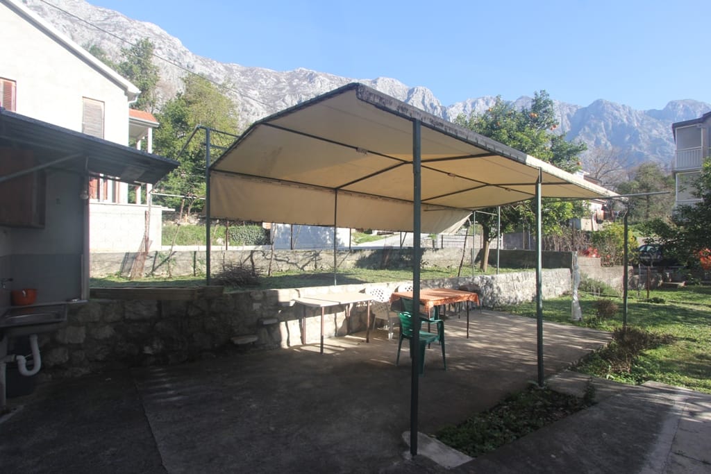 Terrace with a canopy and dining area in the courtyard of a house in Orahovac, Montenegro, with a scenic view of the mountain landscape.