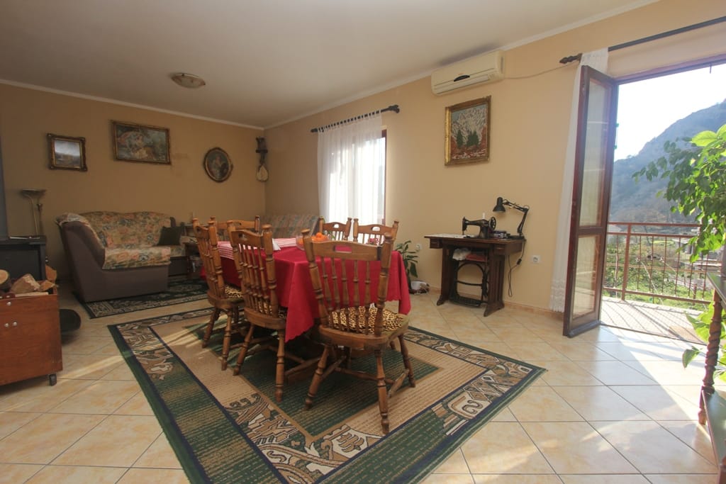 Living room with dining area in a house in Orahovac, Montenegro: wooden furniture, tiled floor, and access to a terrace with a view.