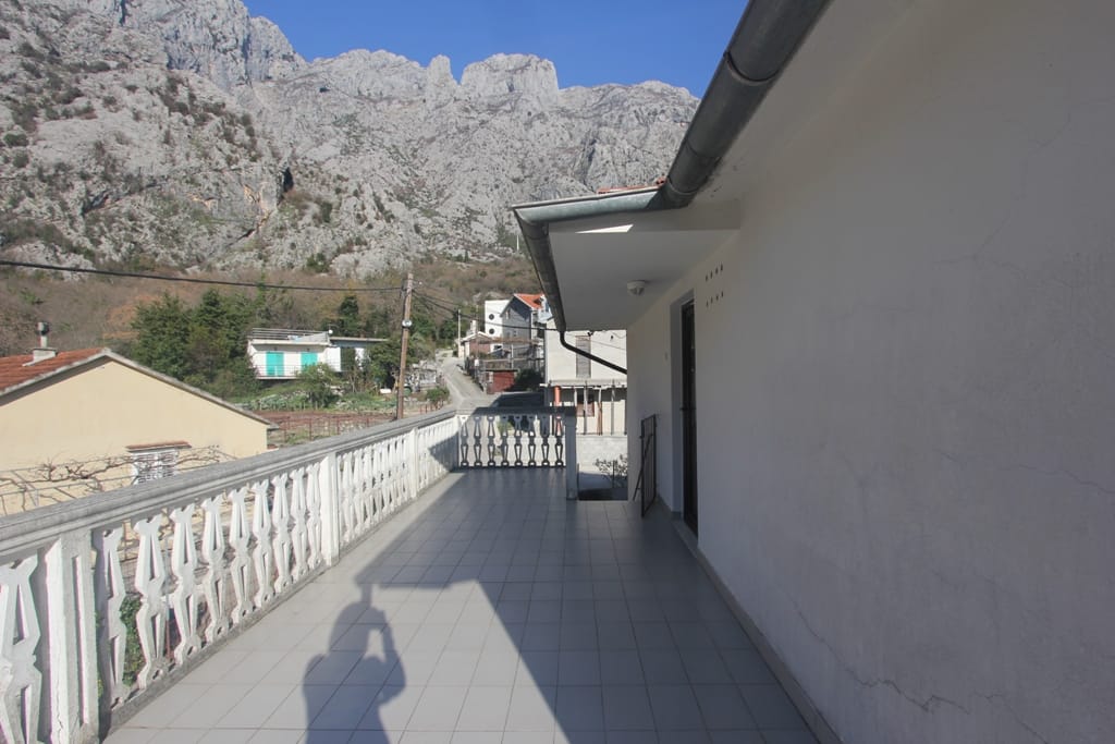 Spacious balcony with balustrade and mountain views in a house, Orahovac, Montenegro. Tiled floor, light-colored facade finish.