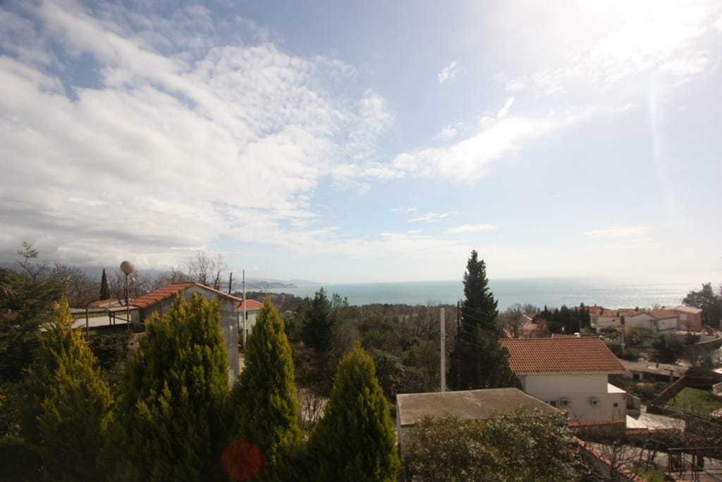 Panoramic sea and mountain view from the house terrace in Sutomore, Montenegro, surrounded by cypress trees and private homes.