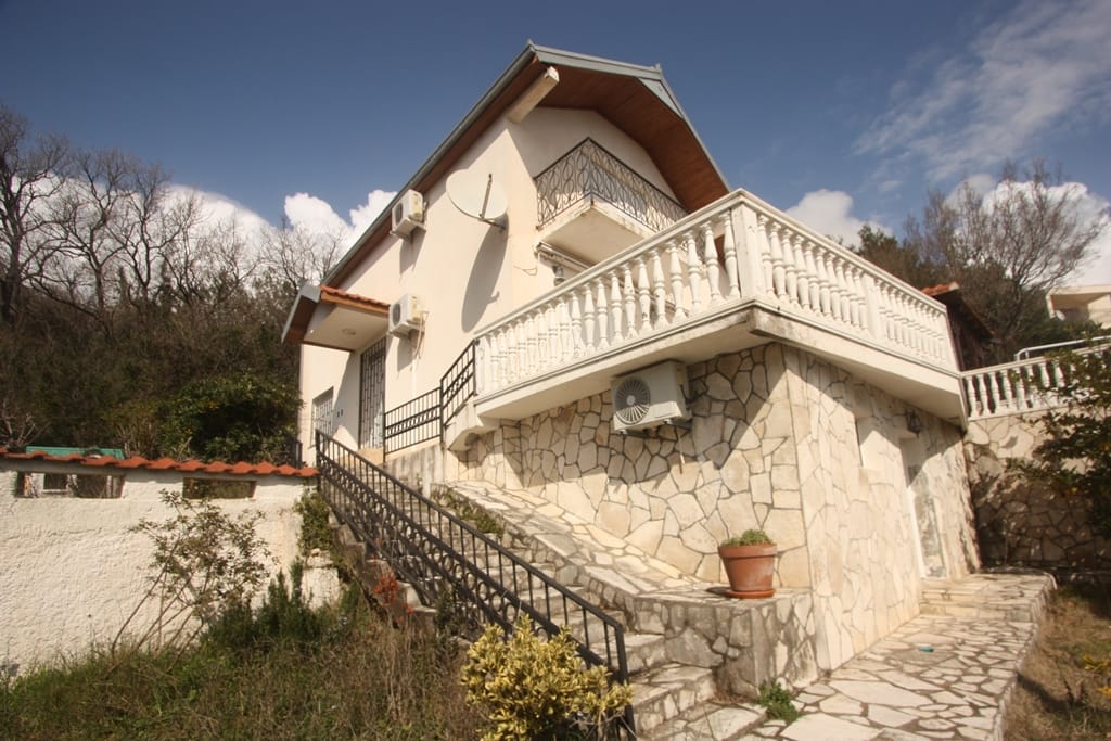 Two-story house in Sutomore, Montenegro: stone-clad facade, balcony with balustrade, and stairs to the plot.