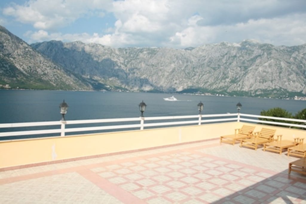 Hotel terrace in Stoliv, Montenegro: view of Kotor Bay, mountains, and sun loungers on a tiled terrace.