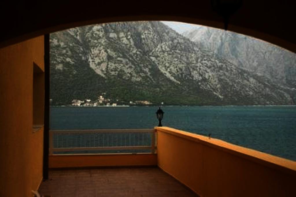 View from the hotel balcony in Stoliv, Montenegro: a panorama of the Bay of Kotor and the mountains, a terrace with yellow walls.