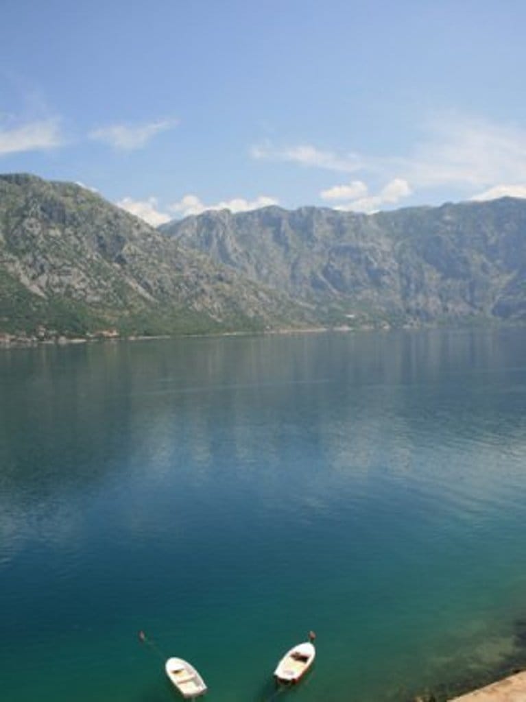 Panoramic view of Kotor Bay and the mountains from a hotel in Stoliv, Montenegro, with boats on the calm water.