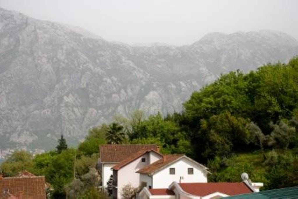 Mountain and hotel view in Stoliv, Montenegro: white buildings with tiled roofs among greenery and a mountain landscape.