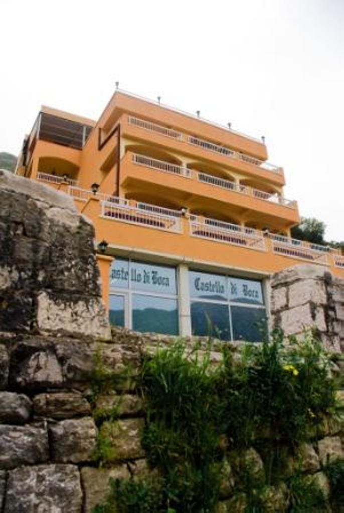 Facade of the Castello di Boca hotel in Stoliv, Montenegro: a multi-story building with terraces and stonework at the entrance.