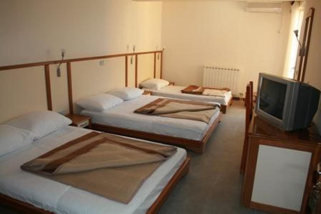 Triple room in the Stoliv hotel, Montenegro: three beds with white linens, wooden furniture, and a TV.