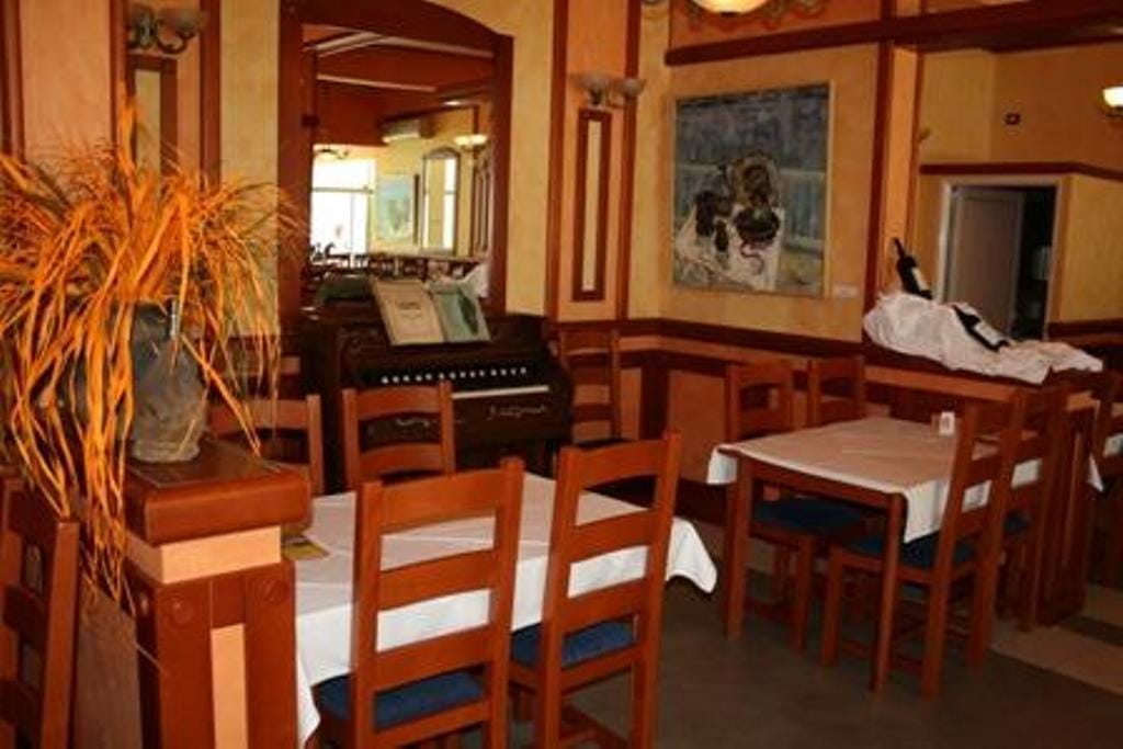 Hotel restaurant interior in Stoliv, Montenegro: wooden furniture, white tablecloths, and an antique piano in the dining room.