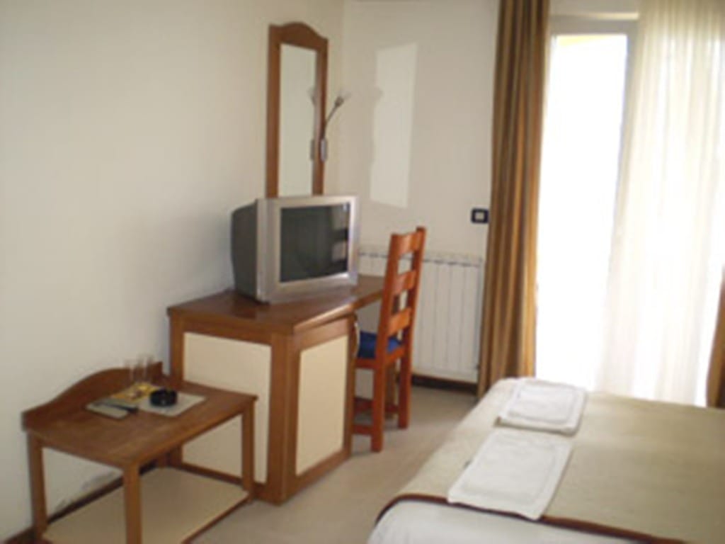 Bedroom interior at Stoliv Hotel, Montenegro: wooden furniture, TV, mirror, and access to the balcony with curtains.