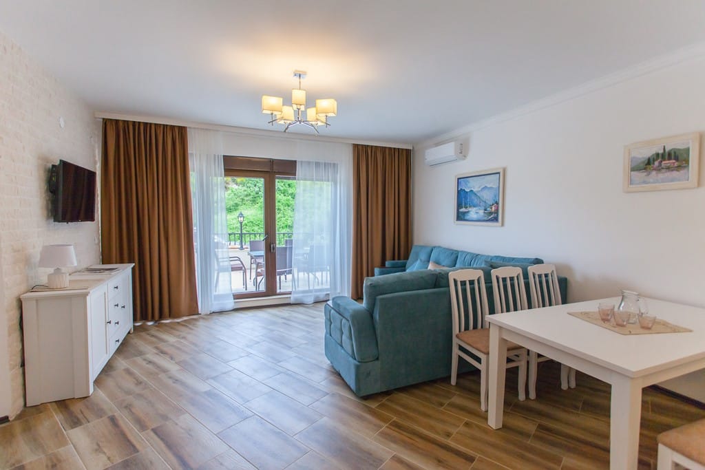 Living room in an apartment in Kamenovo, Montenegro: blue sofa, dining area, access to the terrace, and a bright interior.