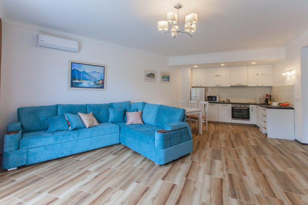 Living room with a blue corner sofa and a modern kitchen in an apartment, Kamenovo, Montenegro. Bright interior with tile flooring.