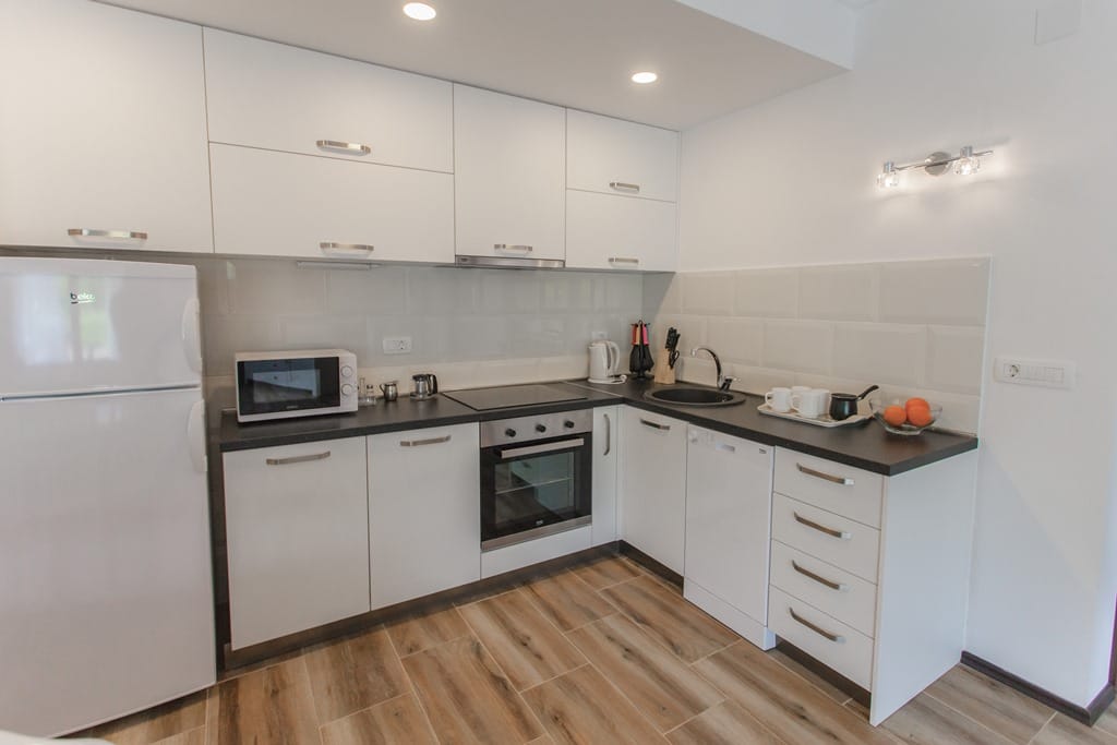 Modern white kitchen in an apartment in Kamenovo, Montenegro: built-in appliances, dark countertop, and tiled floor.