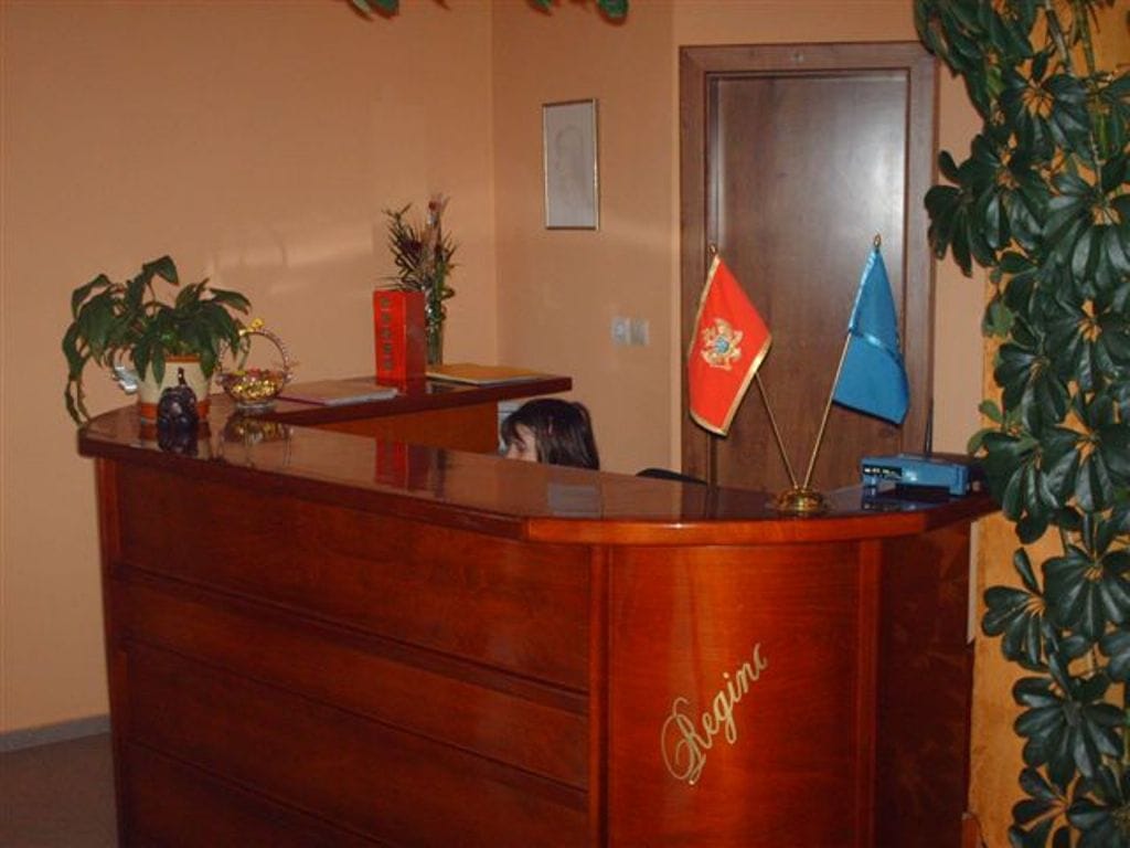 Hotel Regina reception desk in Bijela, Montenegro: a wooden front desk with flags and potted plants in the interior.