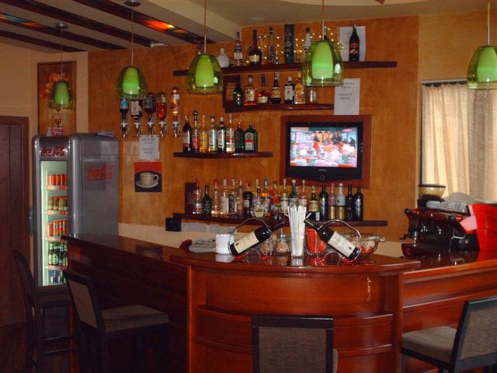 Interior of the bar area at the Biela Hotel, Montenegro: wooden counter, high stools, shelves with drinks, and a TV panel.