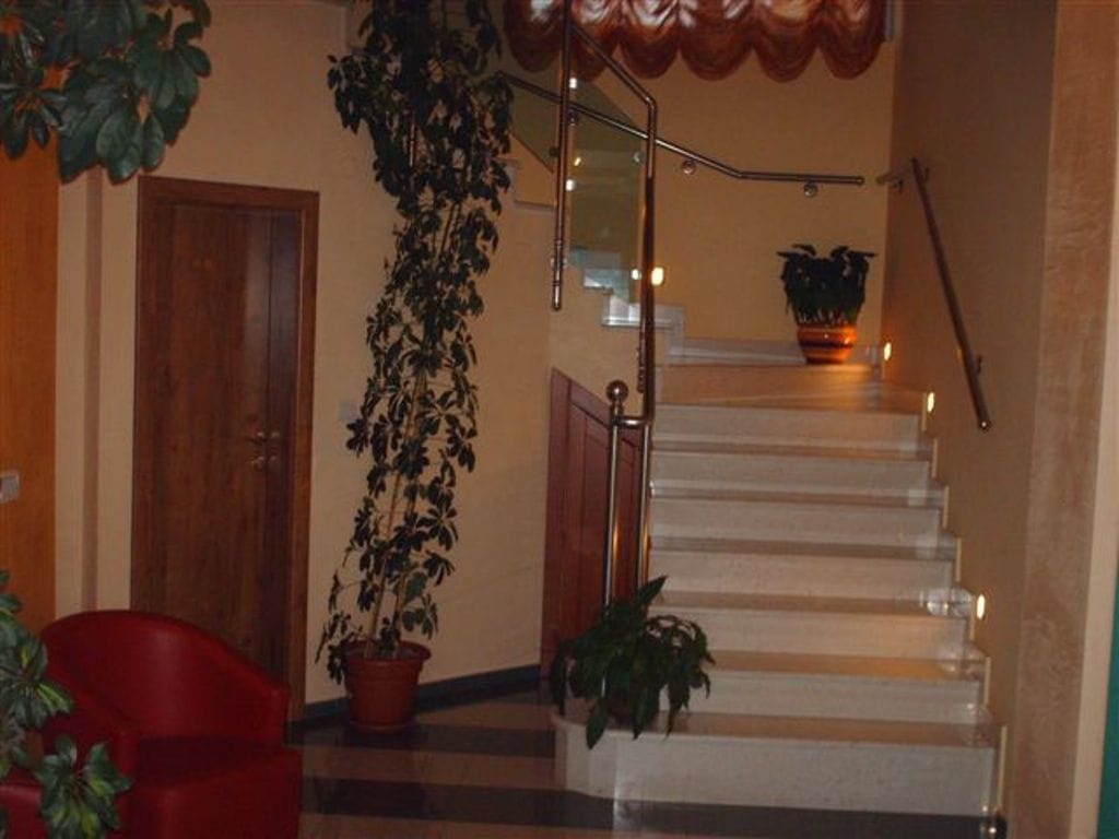 Interior of the mini-hotel lobby in Bijela, Montenegro: marble staircase with lighting, glass railings, and indoor plants.