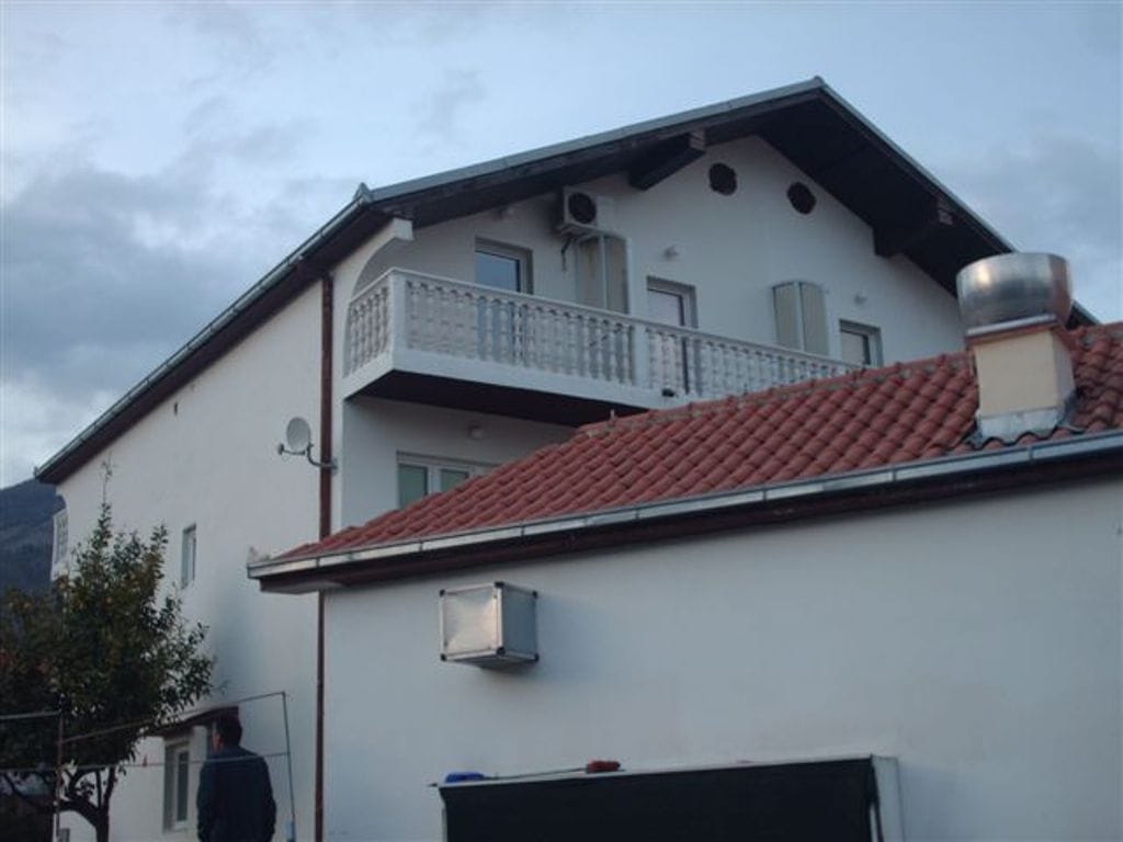 Facade of a mini-hotel in Bijela, Montenegro: a two-story building with white walls, a balcony, and a tiled roof.