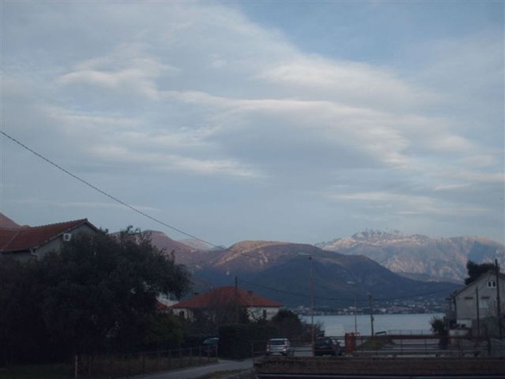 View of the mountains and sea from a mini-hotel in Bijela, Montenegro: a panorama with houses, a road, and a cloudy sky.