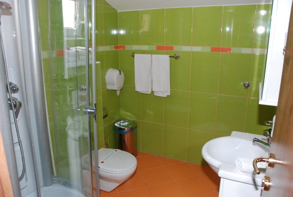 Bathroom with shower cabin in a mini-hotel, Bijela, Montenegro: bright tiles, fixtures, and towels.
