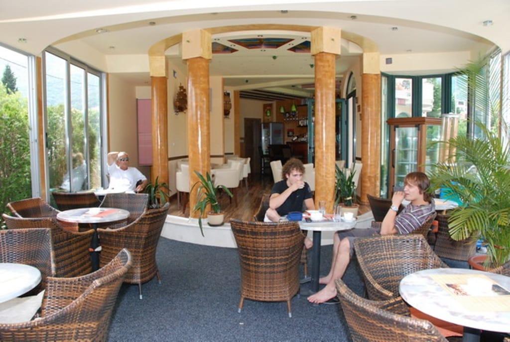 Cafe interior in the Biela mini-hotel, Montenegro: wicker chairs, decorative columns, and panoramic glazing.