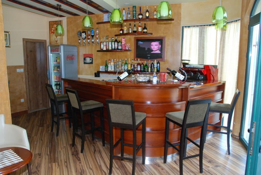 Interior of the bar area in a mini-hotel, Bijela, Montenegro: wooden bar counter, high stools, and a beverage refrigerator.