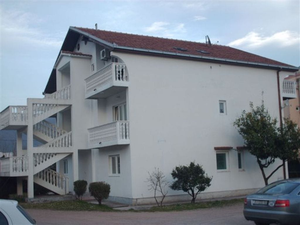 Three-story mini-hotel in Bijela, Montenegro: a white building with a tiled roof, balconies, and an exterior staircase.