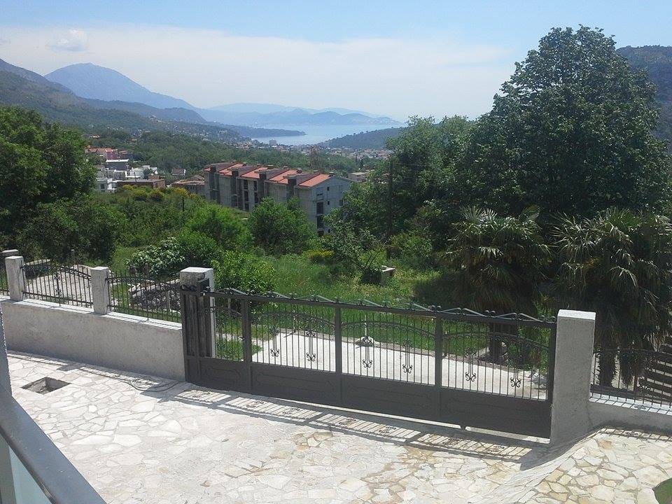 Sea and mountain view from the villa grounds in Sutomore, Montenegro: wrought-iron gate, stone terrace, and green garden.