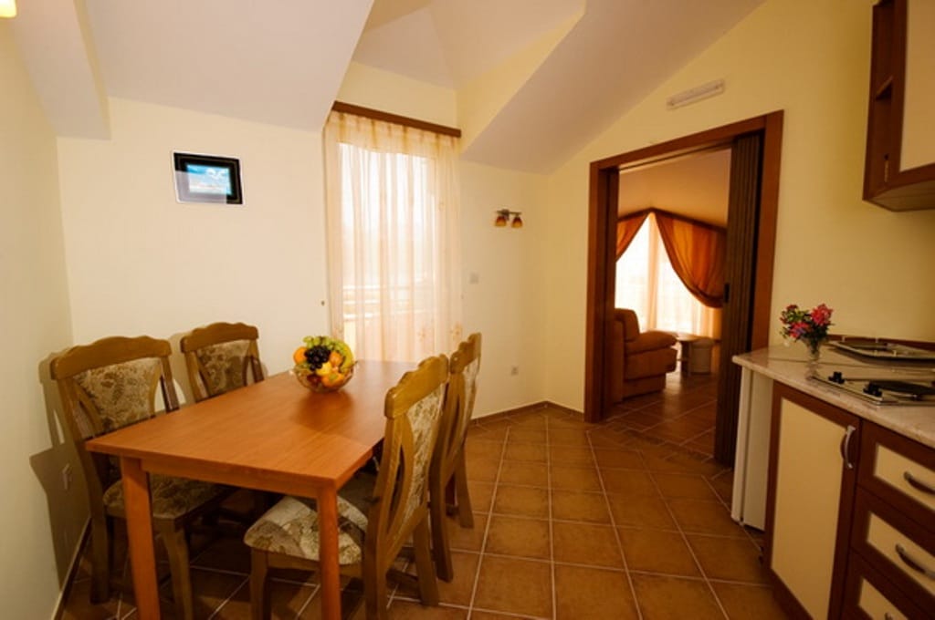 Kitchen with dining area in a mini-hotel, Bijela, Montenegro: wooden table, tiled floor, and a view into the living room.