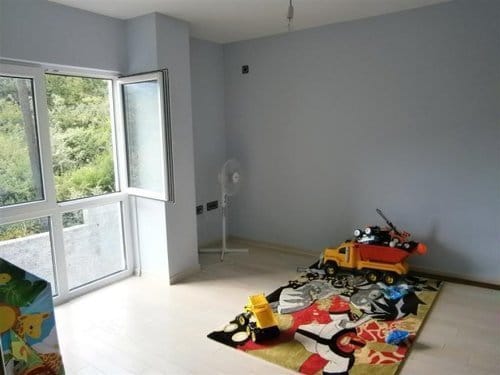 Bright bedroom with a panoramic window and a view of greenery in a villa, Sutomore, Montenegro. Children's room with a play rug.