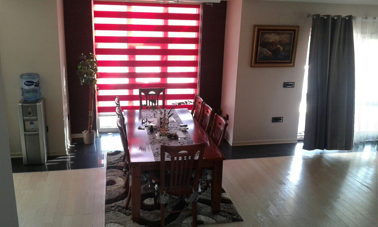Living room with dining area in a villa in Sutomore, Montenegro: wooden table, chairs, and panoramic windows with blinds.