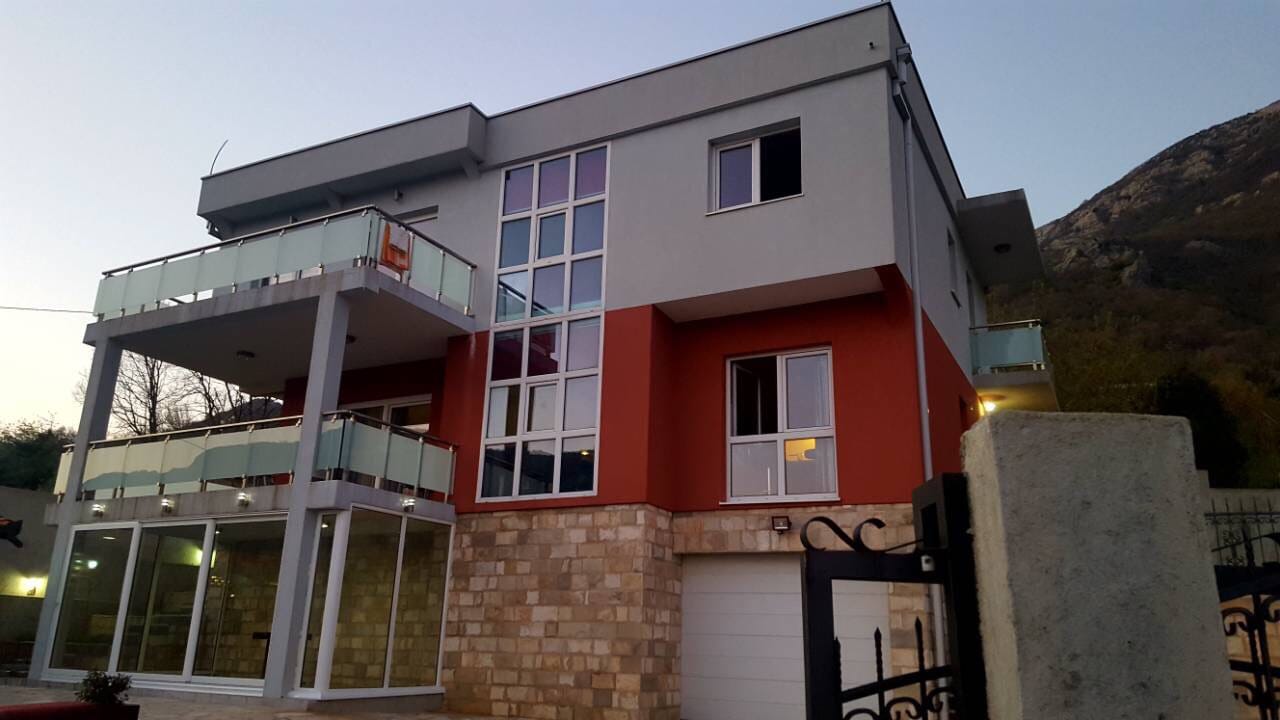 Modern two-story villa in Sutomore, Montenegro: panoramic glazing, stone cladding, and balconies with railings.
