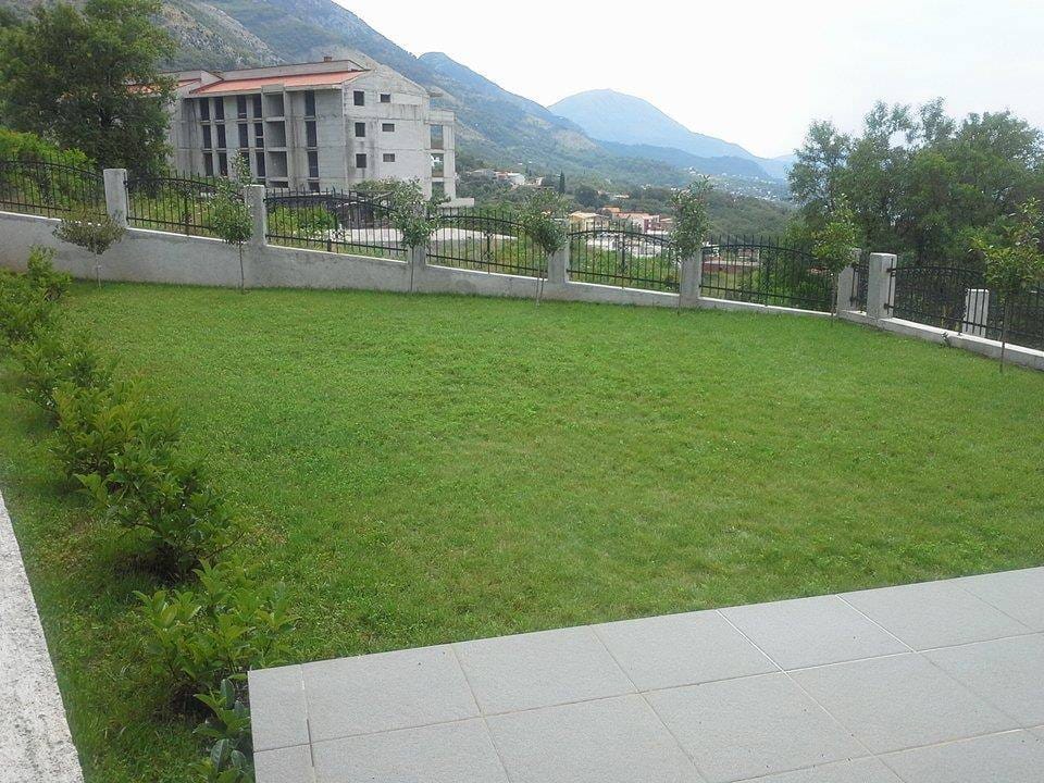 Well-kept green lawn on the private grounds of a villa in Sutomore, Montenegro, with mountain views and fencing.