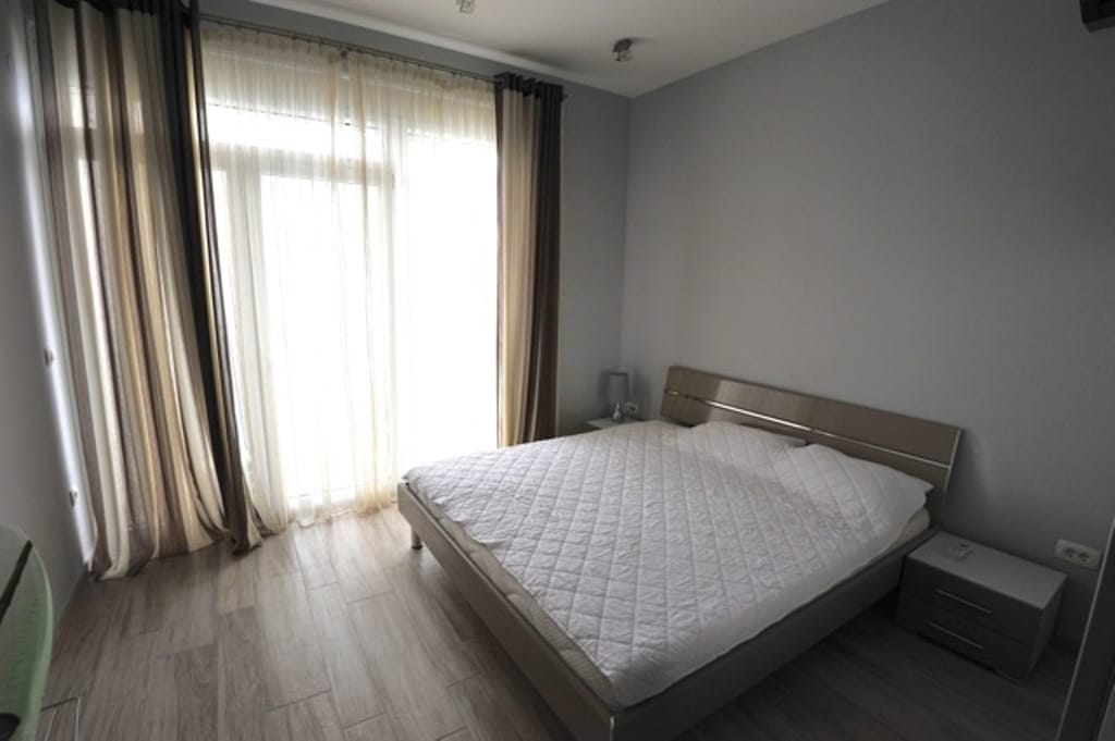 Bright bedroom with a double bed in an apartment in Dobri Vody, Montenegro: panoramic window and modern interior.