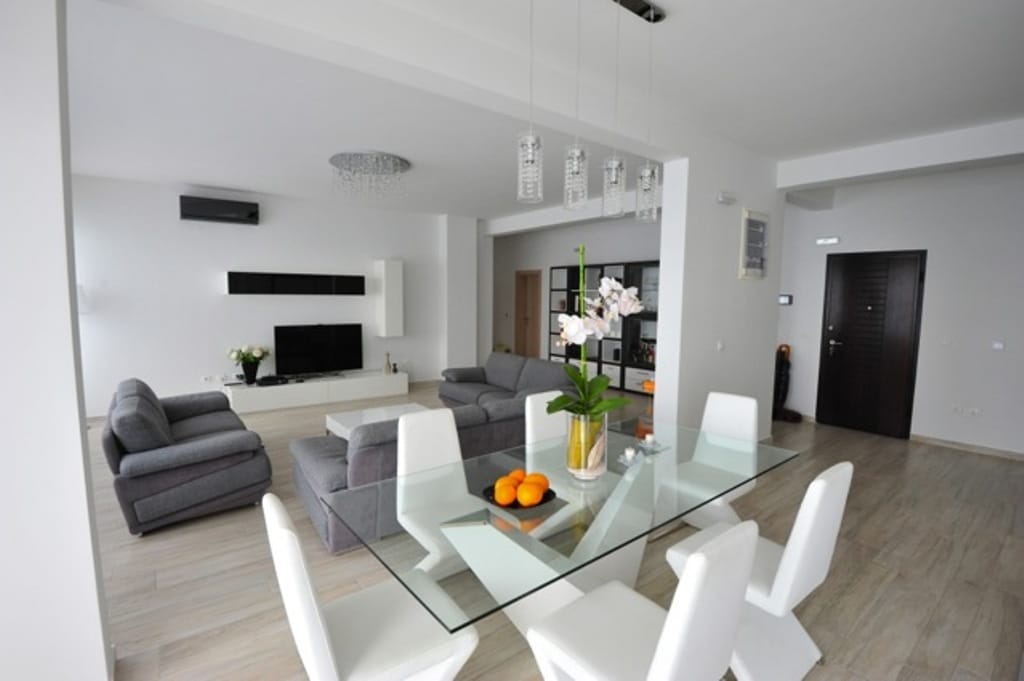 Modern living room with dining area in an apartment, Dobri Vody, Montenegro: glass table, gray sofas, and light flooring.