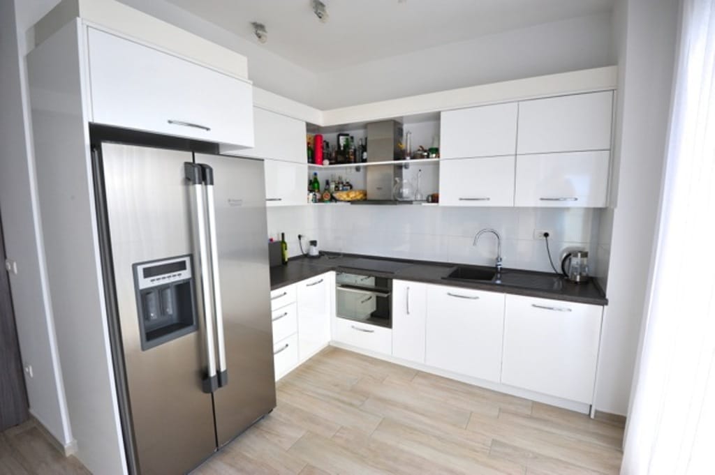 Modern white kitchen with appliances in an apartment in Dobri Vody, Montenegro: glossy fronts and a large refrigerator.